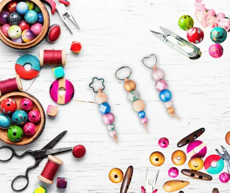 Glenhaven Park Camps A workspace with colorful beads, thread spools, scissors, and beaded earrings in progress on a white wooden surface evokes the spirit of camp craft activities, brimming with creativity.